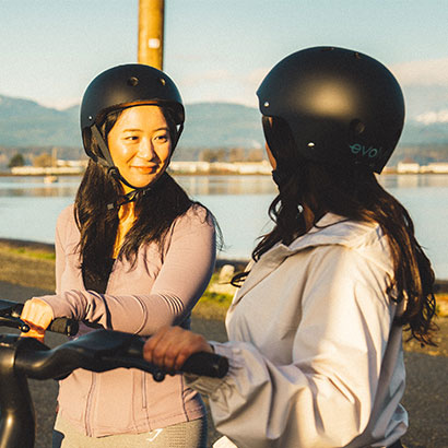 Friends chatting while holding an e-scooter and wearing helmets